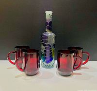 Group shot of four ruby red glass mugs and decorated decanter