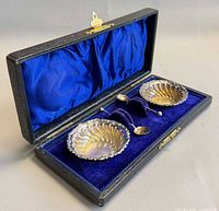 Open case displaying two sterling salt cellars and two spoons in blue velvet interior