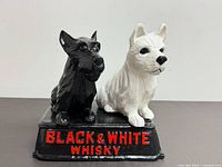 Front view of black Scottish Terrier and white West Highland Terrier figurine on base with Black & White Whisky lettering
