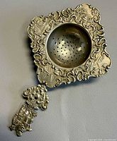 Front view showing ornate repoussé border, perforated bowl, decorative handle