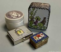 Four trinket boxes grouped: ceramic round, enamel grapevine, silver-tone crest, brass micro-mosaic
