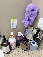 Countertop view showing all soap bottles, cup dispenser, mirror, bath pouf