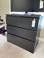 Front view of black three-drawer dresser with glass top and TV on top