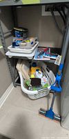 Overall view of bottom two shelves showing laundry basket, mop and cleaning supplies