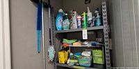 Full view of metal shelving unit with cleaning bottles, cloths and other supplies
