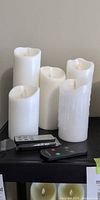 Five white pillar candles and two remotes on shelf