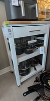 Full view of white kitchen cart with drawer, wire basket, shelf and casters