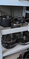 Five KitchenAid cookware pieces on shelf showing lids and handles