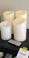 Four ivory flameless pillar candles and remote control on shelf