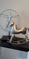 Rocking horse in foreground, human ring sculpture behind