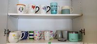Two cupboard shelves showing entire set of ceramic mugs and Yeti mug