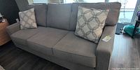 Front view of grey three-seat sofa with two patterned pillows