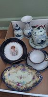 Group view of Delft pieces, teacup set, platter and portrait plate in box