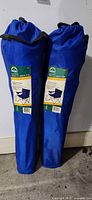 Two blue carry bags containing folding camp chairs standing upright