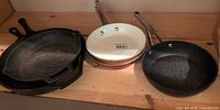 Five pans on shelf: cast iron stacked and three small fry pans