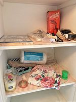 Two-shelf cupboard with boxed stationery, steam iron box, cosmetic bags, apron, absorbent pads, soap, scented disc visible