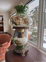 Full view of hurricane lamp on table showing both globes, painted roses, brass base