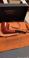 Pipe resting on calfskin pouch inside open Savinelli Autograph box
