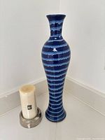 Blue striped ceramic vase standing next to cream candle in metal holder