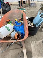 Overall lot showing wheelbarrow filled with garden tools, pots, sprayers and tarp
