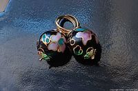 Two cloisonné floral sphere charms with gold rings on dark surface