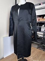 Full front view of black silk overcoat on mannequin