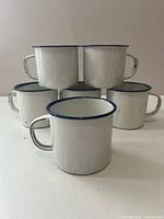 stack of six white enamel mugs with blue rims