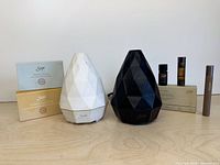 White and black AromaGem diffusers with boxed oil collections and individual roll-ons displayed on tabletop