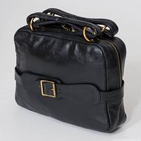 Angled view showing black leather body, gold-tone rings, belt detail, zip closure