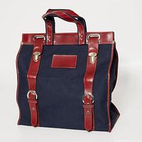 Front view of navy canvas tote with red vinyl straps and buckle hardware