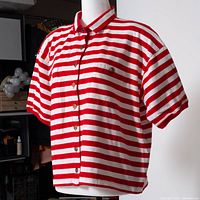 Angled view of red and white striped shirt on mannequin showing collar, gold buttons, pocket, sleeves