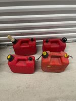 Front view of four red gasoline cans showing caps, spouts and handles