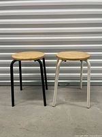 Front view of both stools showing wood seats and black and white legs