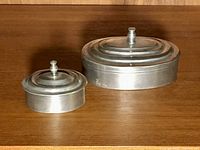 Two oval pewter boxes with lids on wood surface
