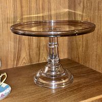 side view of clear glass pedestal cake plate on shelf