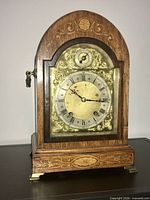 Front view of wood mantle clock showing arched top, brass dial, inlay, missing pendulum visible through glass