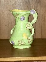 Side view of green ribbed ceramic pitcher with applied flowers