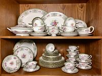 Full service displayed on two wooden shelves showing plates, cups, serving pieces