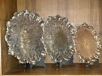 Front view of three graduated ornate silver-plated trays on stands