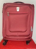 Front view of burgundy Atlantic carry-on showing zip pocket, wheels
