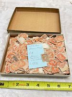 Open box filled with numerous orange 3-cent Queen Victoria stamps with cancellations and blue collector note, tape measure for scale