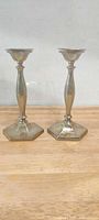 Full view of both matching silver-plated candlesticks standing side by side on wooden surface