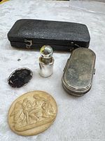 All items laid out: perfume bottle, pill case, carved plaque, photograph, fragment, black case