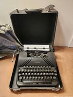 Typewriter seated in open hard case with fabric cover to side