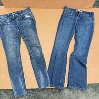 Two pairs of women’s blue jeans laid flat, one distressed bootcut, one darker straight-leg