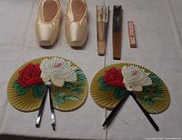 Pair satin pointe shoes, closed and open folding fans arranged on table