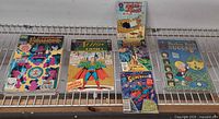 Five stacks of comic books showing titles Excalibur, Action Comics, Superman, Adventure Comics, Sugar & Spike, Richie Rich