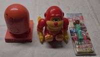 All three items: orange desk figure, red monkey toy, sealed Mater PEZ