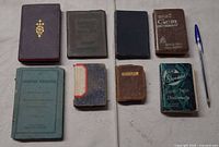 All eight small books laid out with pen for scale
