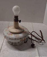 Overall view of milk glass lamp base with bulb and cord visible